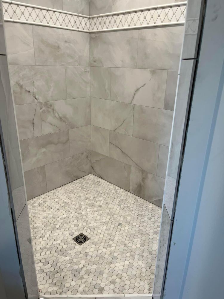 A walk in shower with marble tiles and a drain.