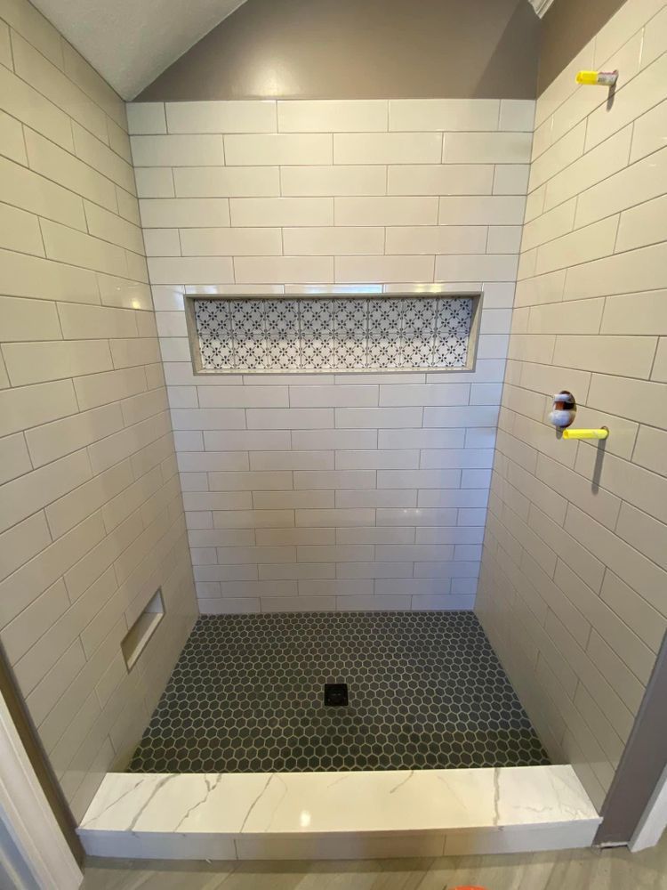 A shower with white tiles and a black tile floor