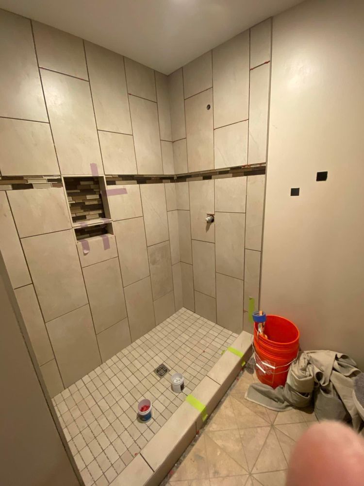 A bathroom with a walk in shower and a red bucket on the floor.