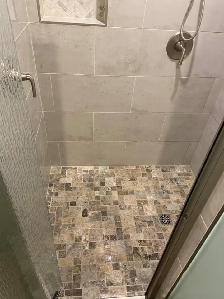 A walk in shower with a tiled floor and a glass door.