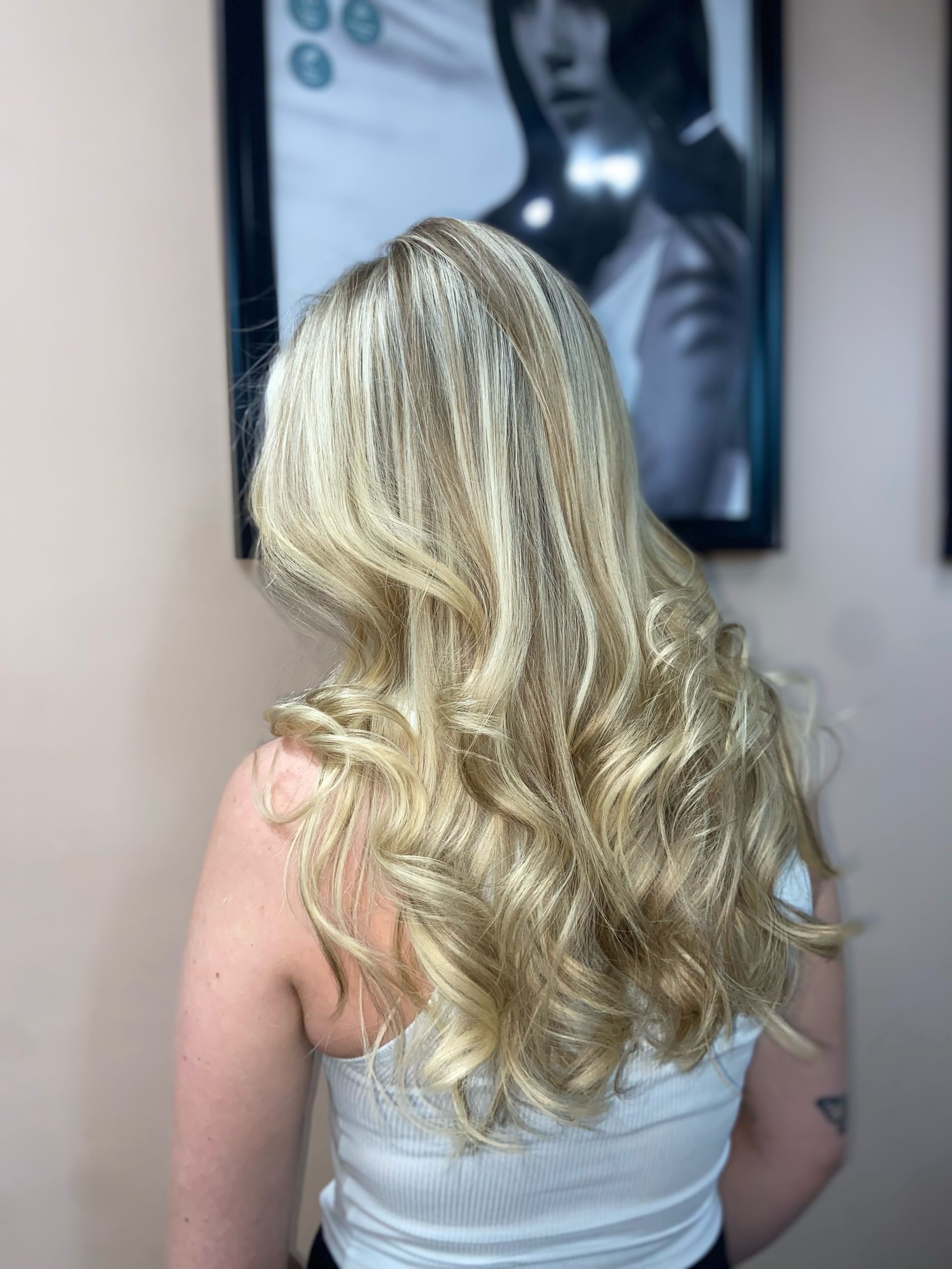 A woman with long blonde hair is standing in front of a brick wall.