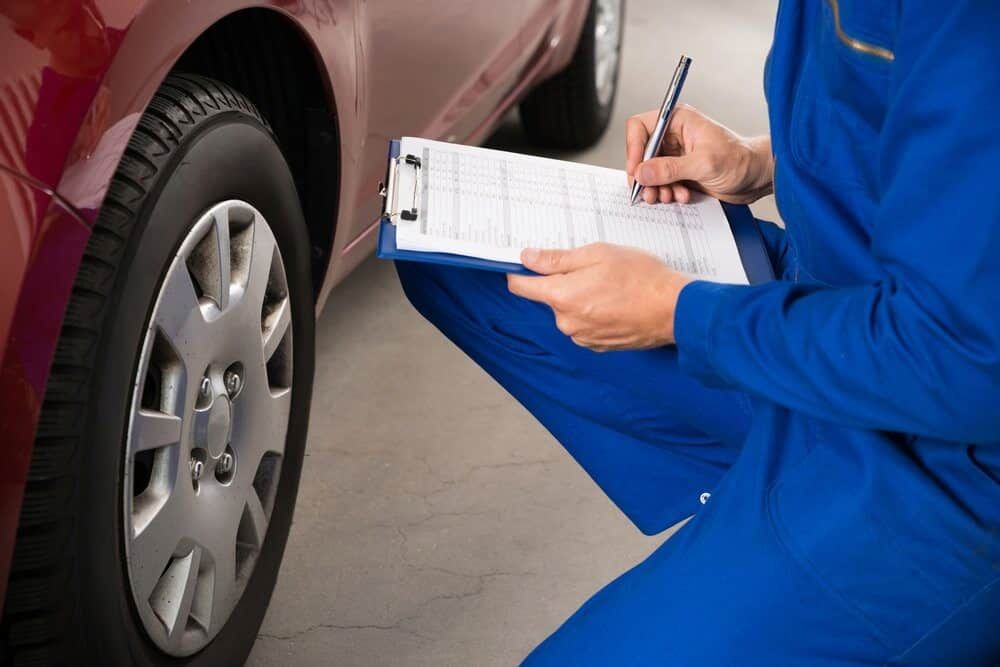 A Mechanic Is Writing On A Clipboard In Front Of A Car — Wayne Devlin Mechanical In Bundaberg Central, QLD