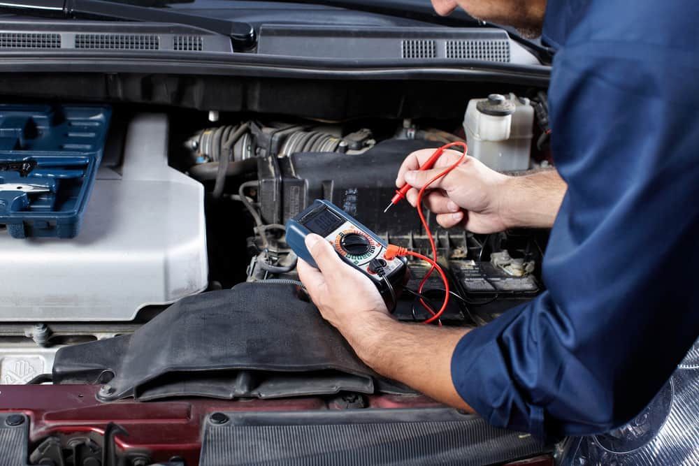 A Man Is Working On A Car Engine With A Multimeter — Wayne Devlin Mechanical In Bundaberg Central, QLD