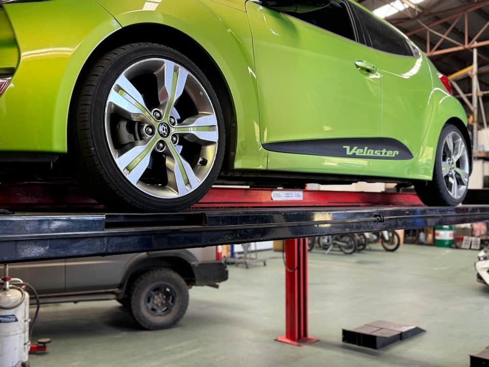A Green Car Is Sitting On A Lift In A Garage — Wayne Devlin Mechanical In Bundaberg Central, QLD