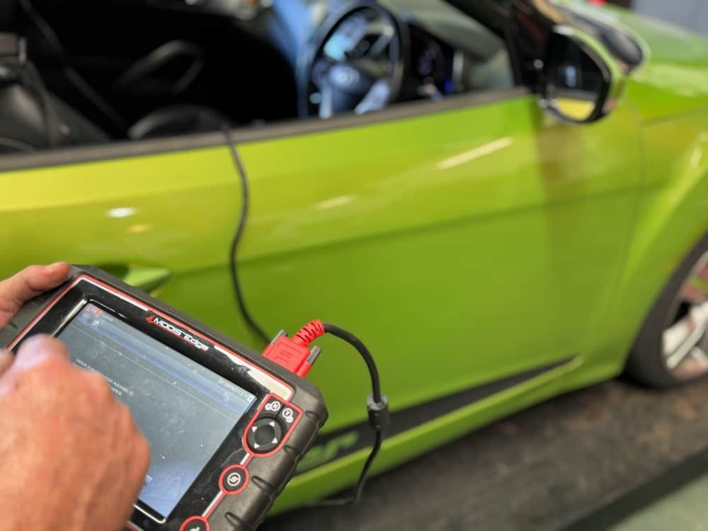 A Person Is Holding A Device In Front Of A Green Car — Wayne Devlin Mechanical In Bundaberg Central, QLD