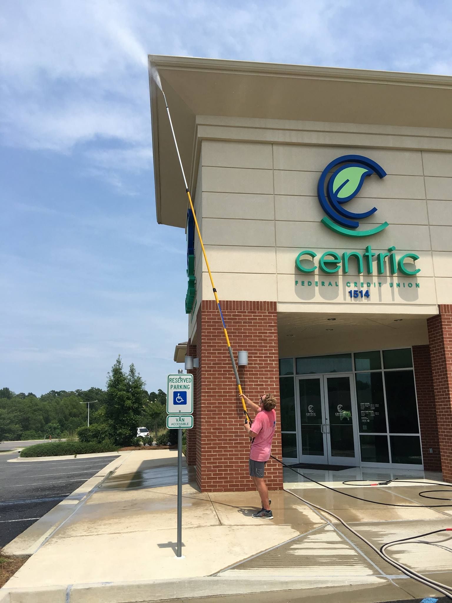 A woman is spraying water on the sidewalk in front of a building.