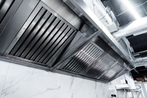 A stainless steel exhaust hood is hanging from the ceiling in a kitchen.