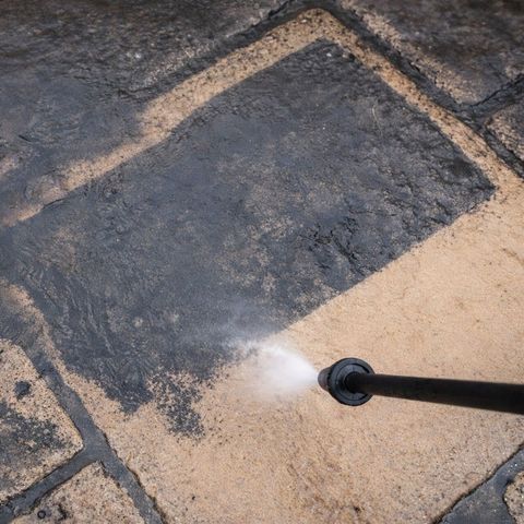 An image of pressure washing. The stream of water is cleaning the patio block.