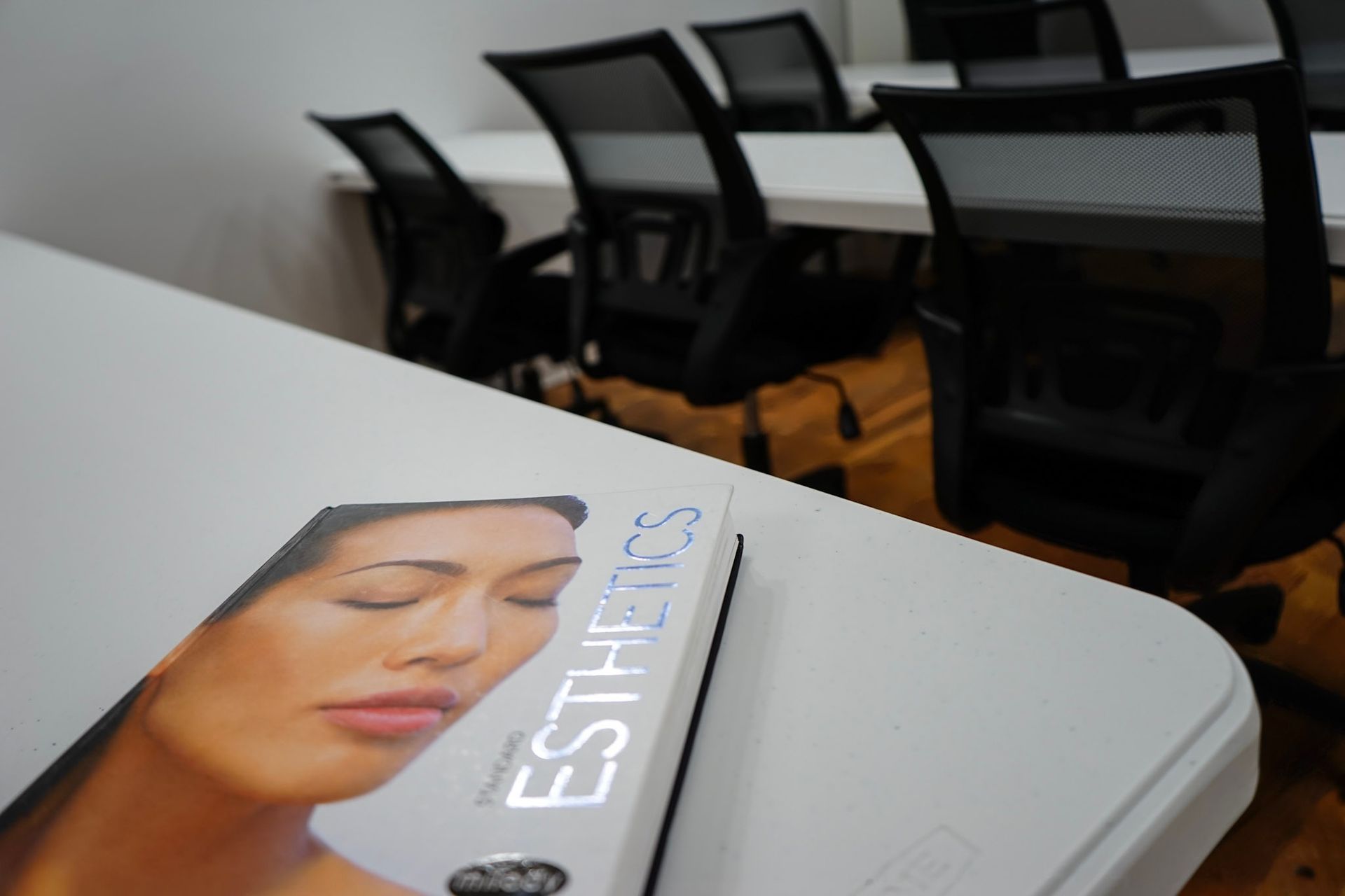 An esthetics textbook on a white table in a classroom with black student chairs and a whiteboard.