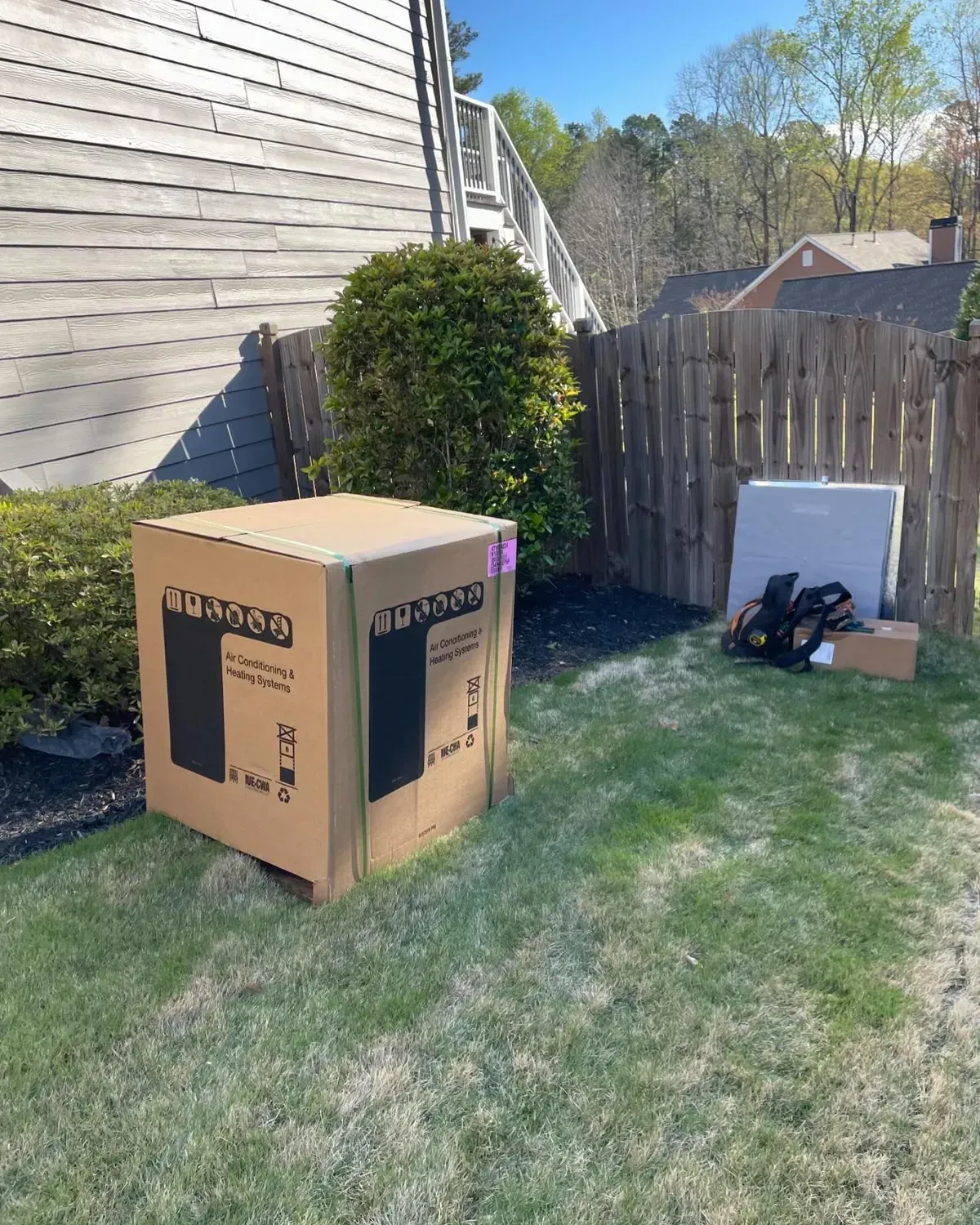 A cardboard box is sitting in the grass in front of a wooden fence.