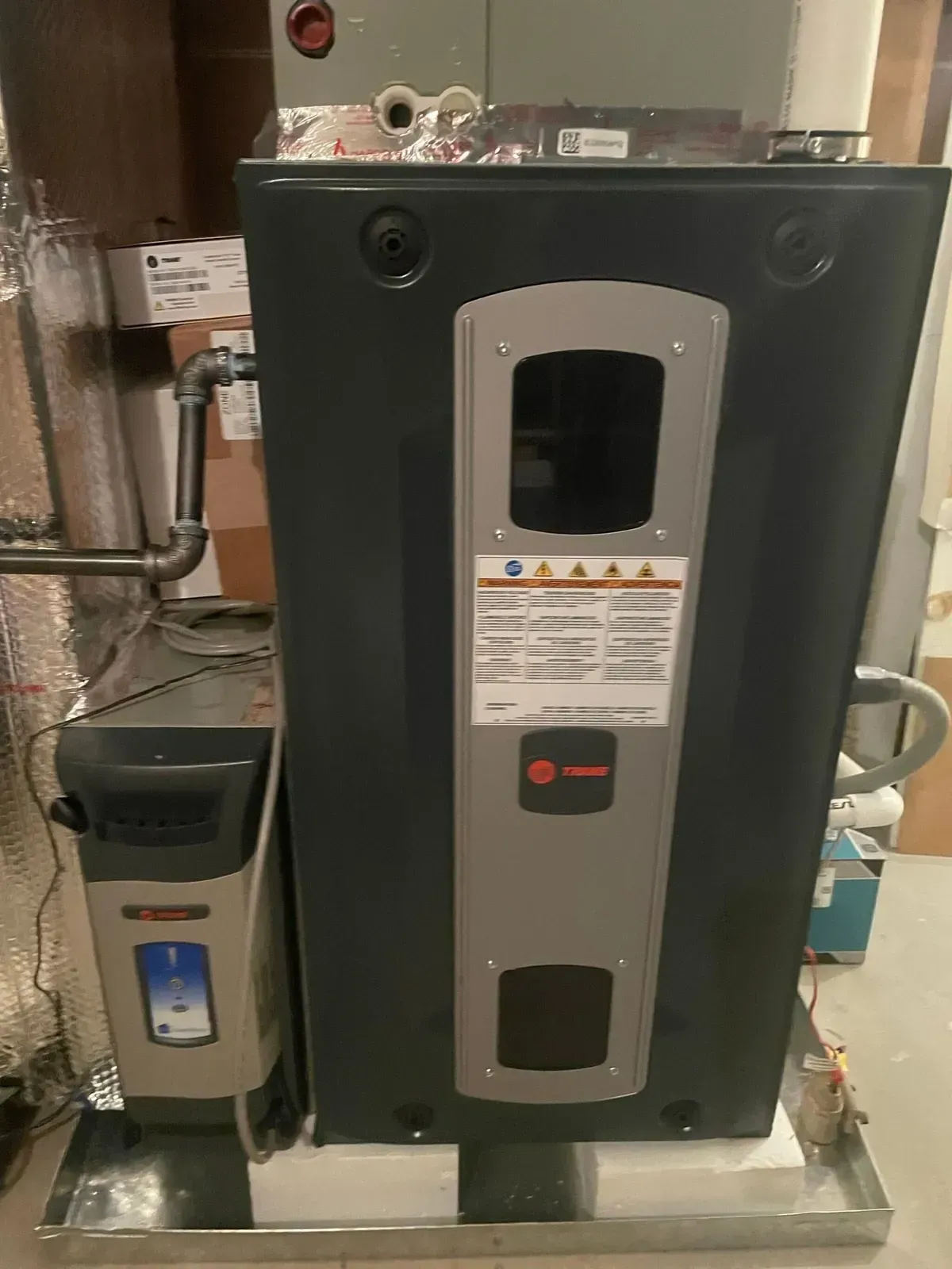 A large boiler is sitting in a basement next to a heater.