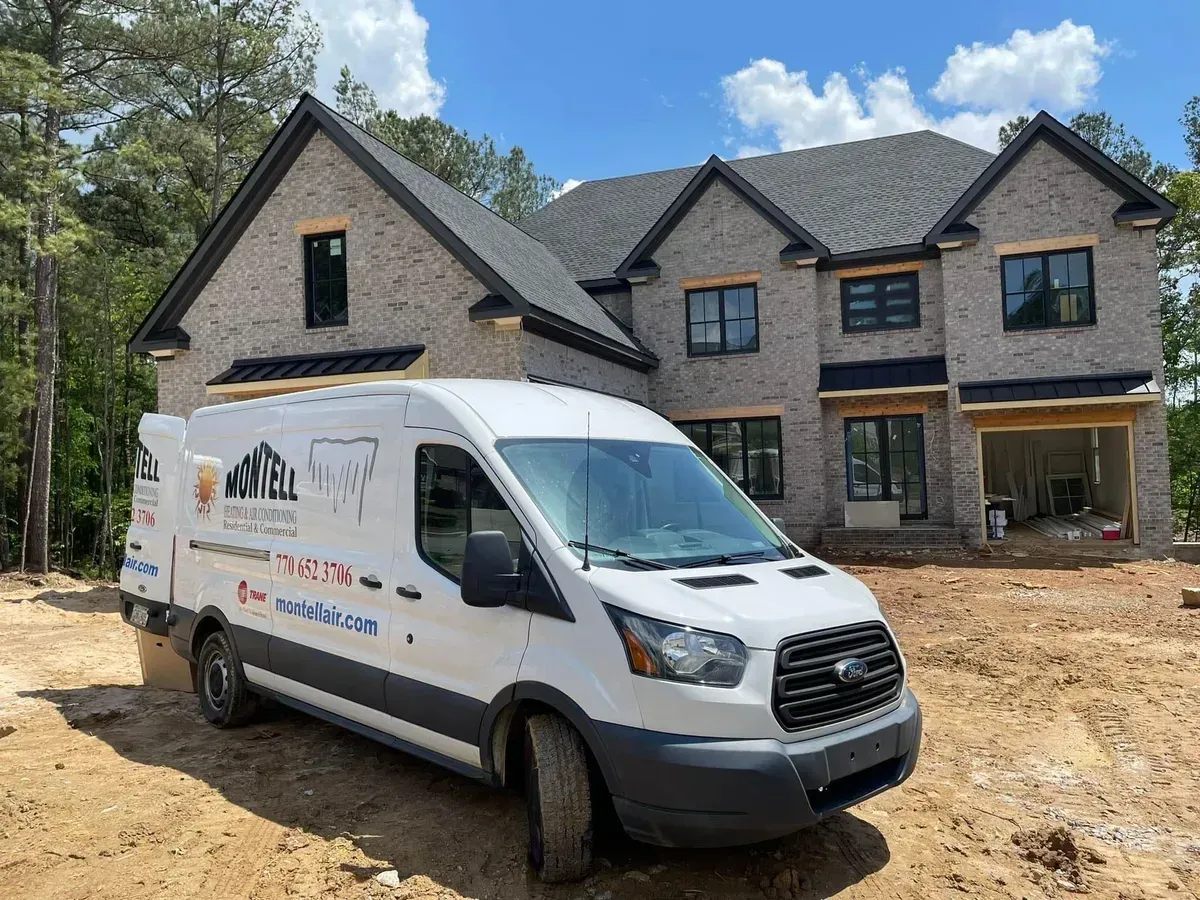 A white van is parked in front of a large brick house under construction.