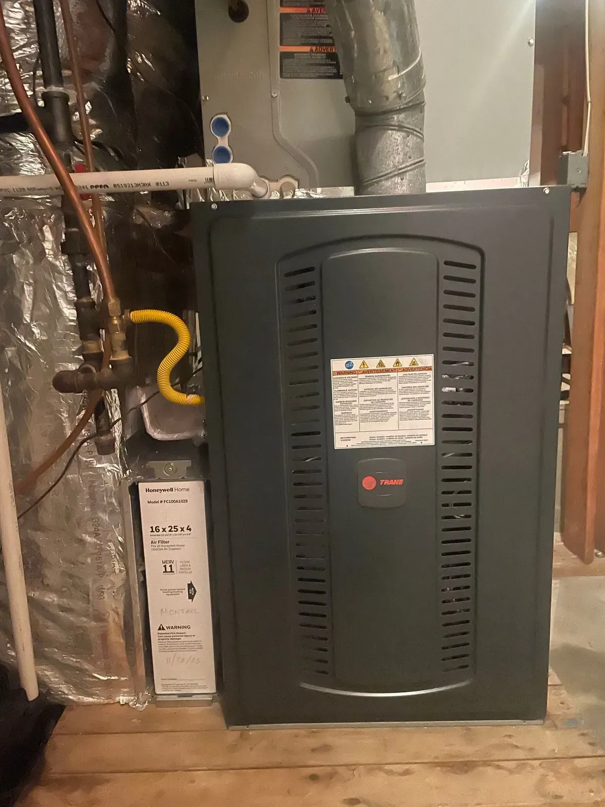 An air conditioner is sitting in a basement next to a pipe.