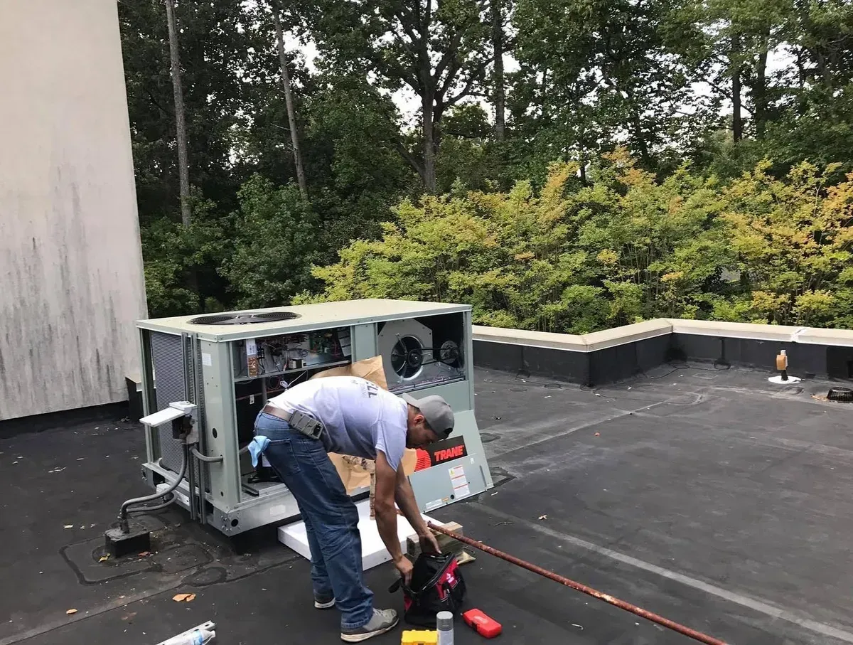 A man is working on an air conditioner on the roof of a building.