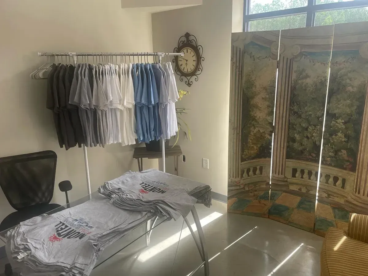 A room with a clock on the wall and a table with clothes on it.