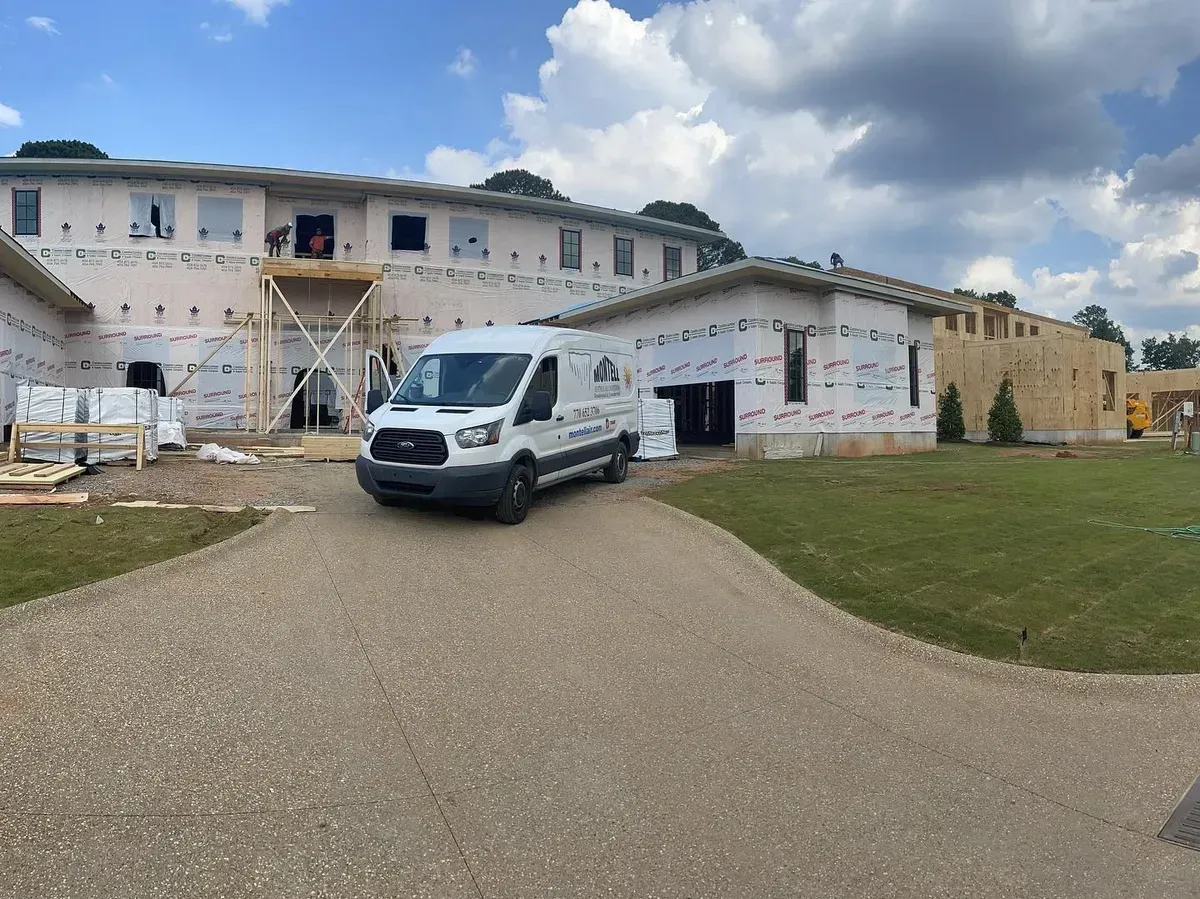 A white van is parked in front of a large building under construction.