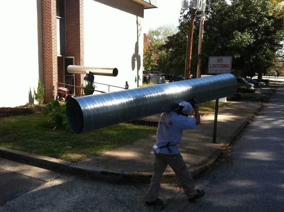 A man is carrying a large metal pipe on his back