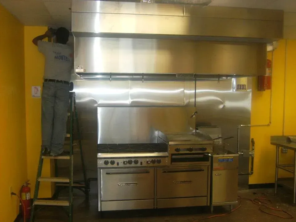 A man standing on a ladder in front of a stainless steel stove