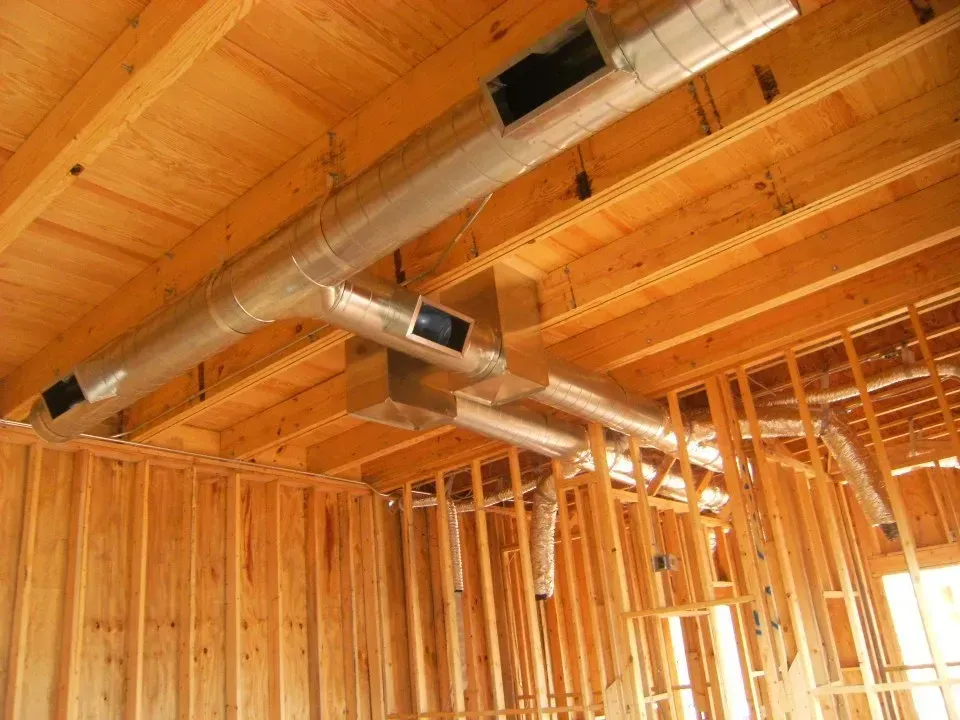 A room in a house under construction with a lot of pipes coming out of the ceiling.
