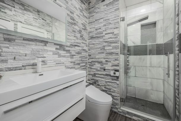 A bathroom with a toilet , sink , mirror and walk in shower.