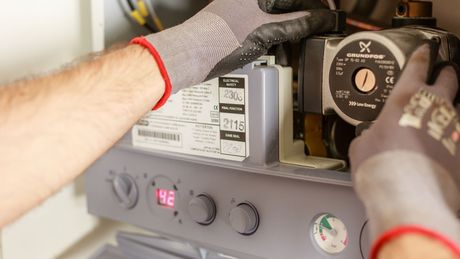 Person in gloves working on a heating system with a control panel, pump, and components.