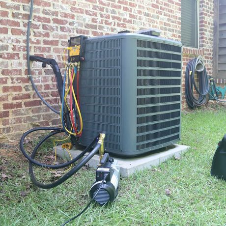 HVAC unit being serviced outdoors. Black hoses connected to gauges, vacuum pump on the ground.