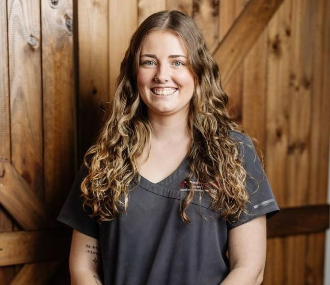 Woman with long curly hair smiles at the camera, wearing a dark gray v-neck shirt — Westlakes Veterinary Hospital in Fennell Bay, NSW