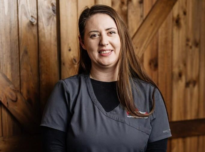Courtney Is Holding a Black Cat in Front of A Wooden Door — Westlakes Veterinary Hospital in Fennell Bay, NSW