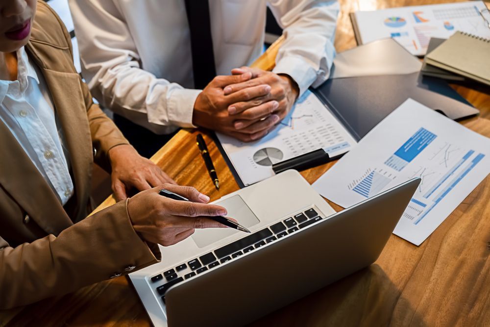 A Man and a Woman Are Sitting at a Table Looking at a Laptop Computer — Peterson Property Valuations In Sunshine Coast, QLD