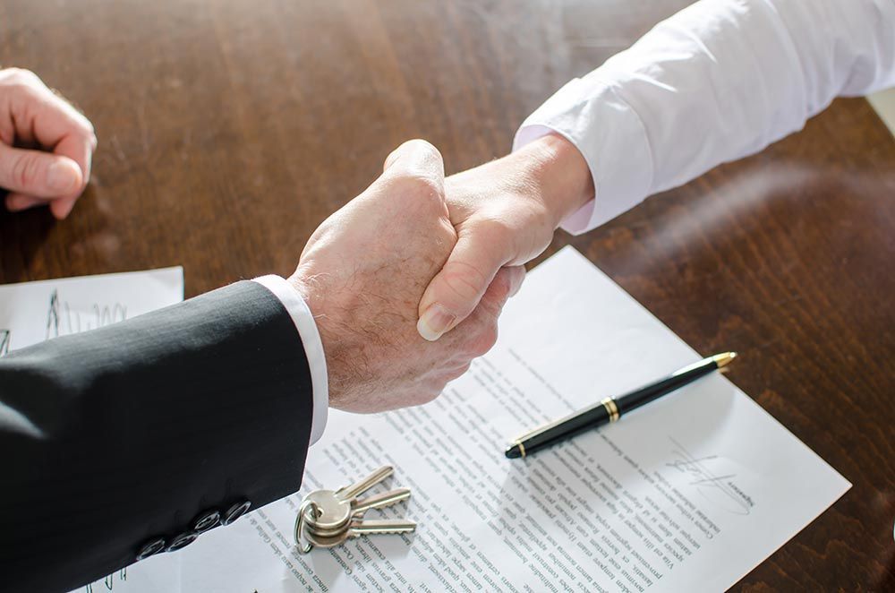 A Man and a Woman Are Shaking Hands Over a Piece of Paper — Peterson Property Valuations In Caloundra West, QLD