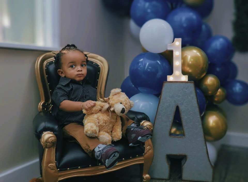 A baby is sitting in a chair holding a teddy bear.