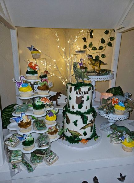 A cake and cupcakes are on a table for a dinosaur birthday party.