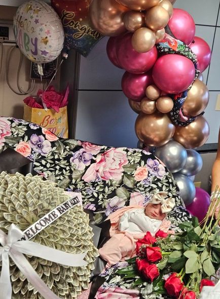 A baby is laying on a bed with balloons and flowers.