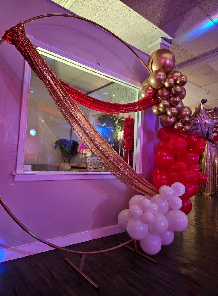 A room decorated with red and gold balloons and a gold hoop.
