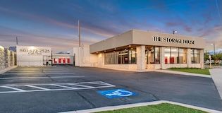 Storage facility with a beige office building, a grey stone wall, and a blue handicap parking space.
