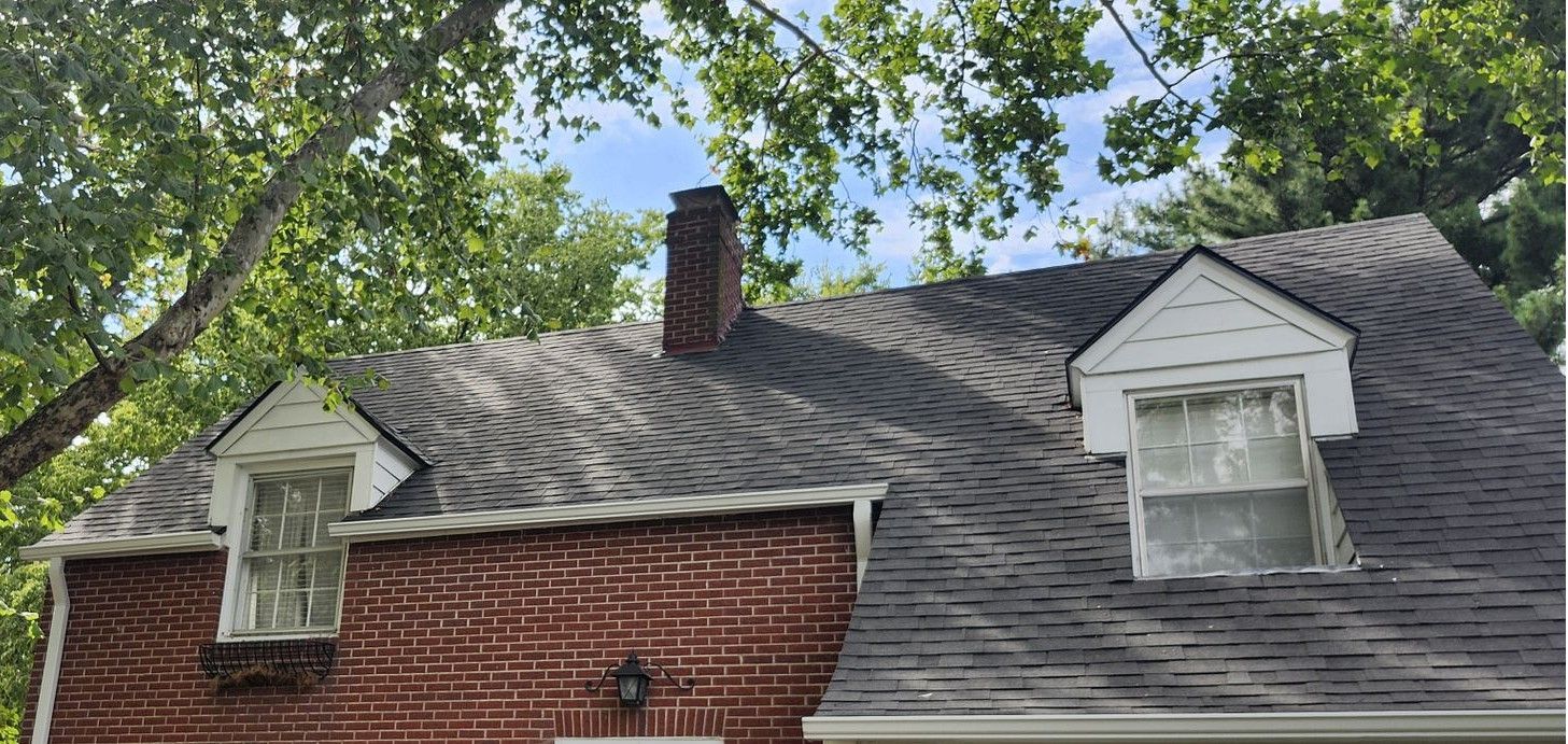 The roof of a brick house with a chimney and two windows.