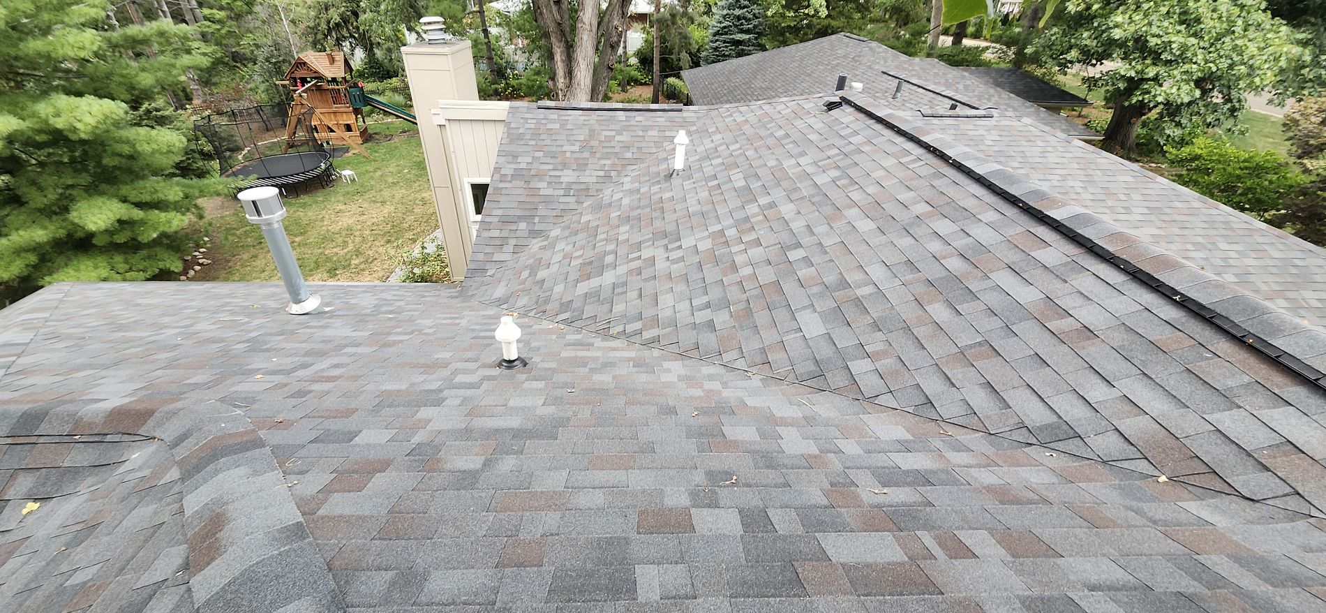 The roof of a house with a gray shingle roof and a chimney.