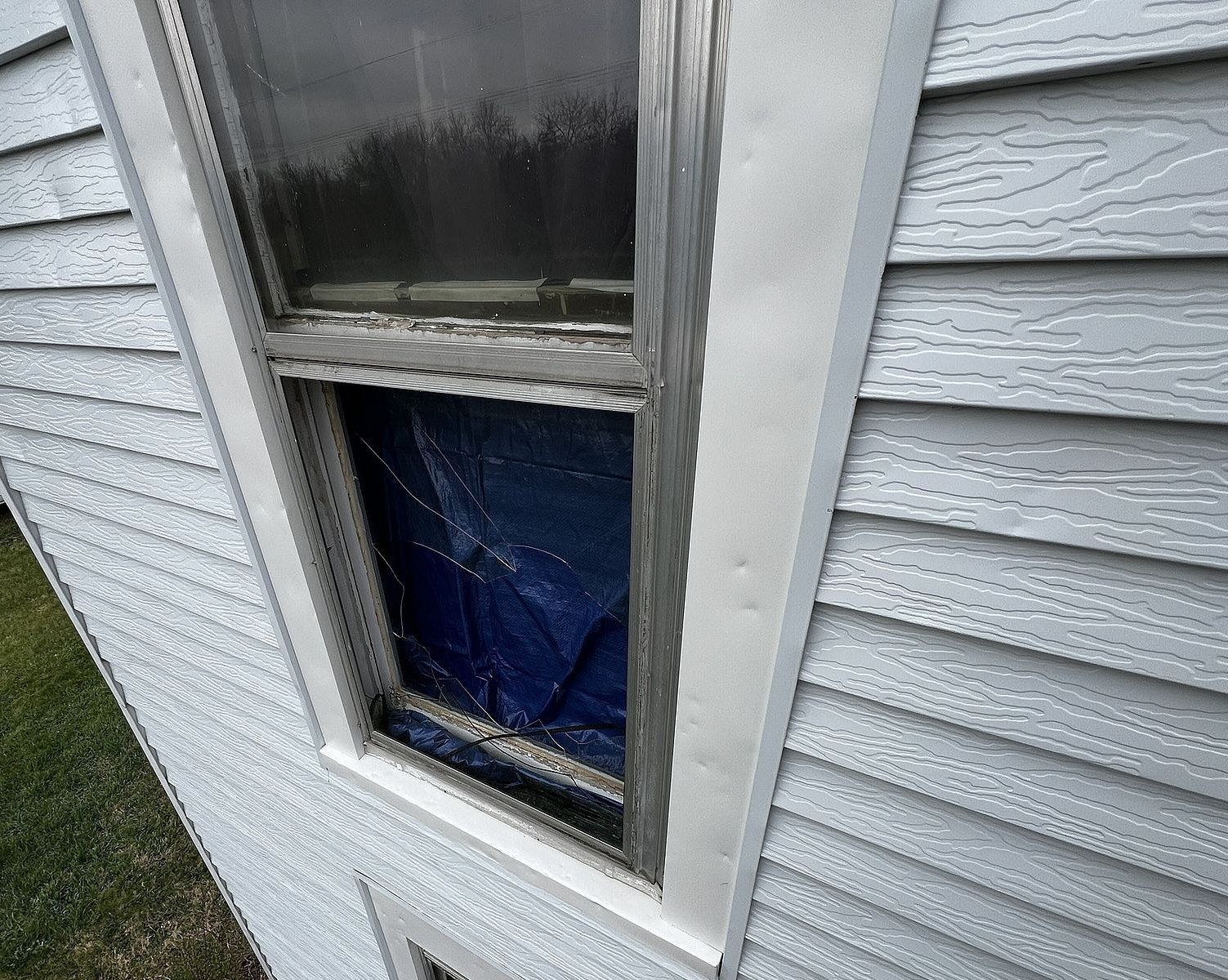 A window on the side of a house with a blue tarp covering it.