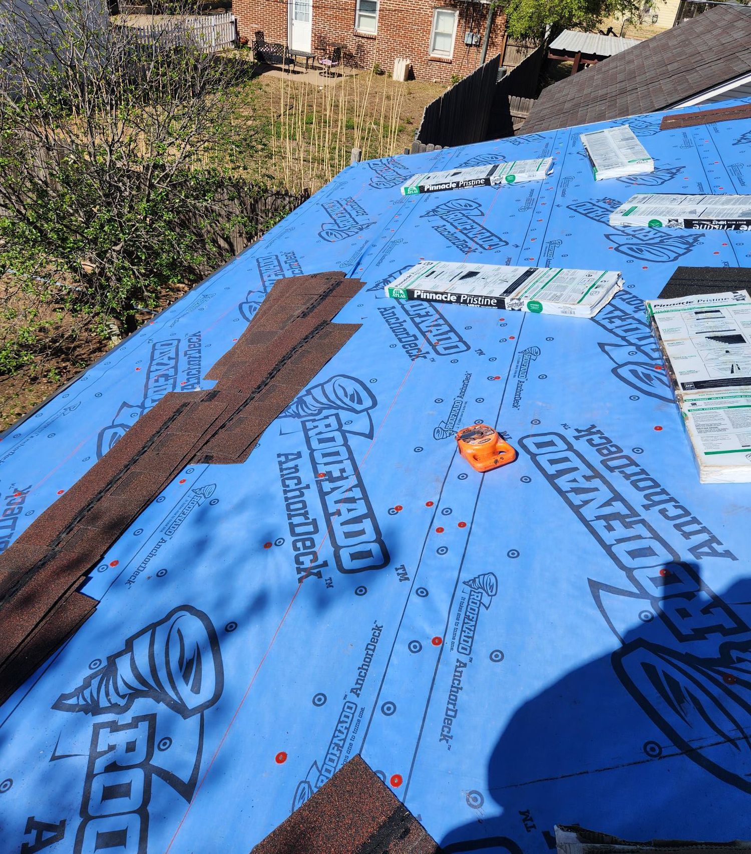 A roof with shingles being installed and a blue tarp covering it