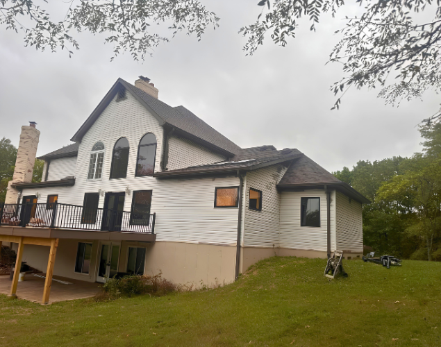 House with white siding and dark roof, seen from a grassy yard on an overcast day.