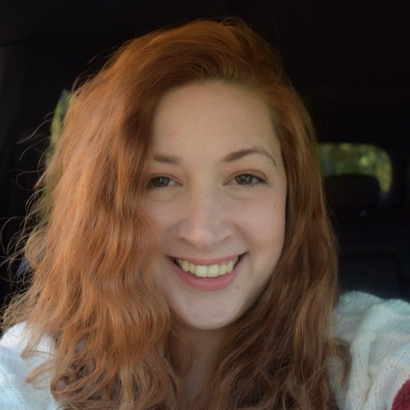 A woman with red hair is smiling while sitting in a car.