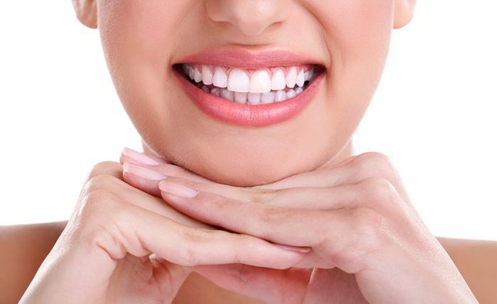 Woman's bright smile with white teeth, hands clasped under her chin.