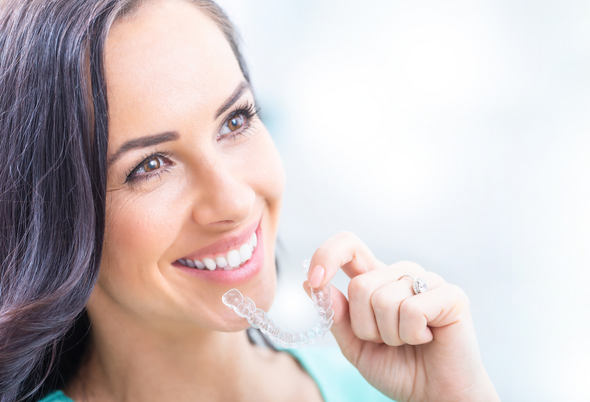 A woman is smiling while holding a clear brace in her mouth.