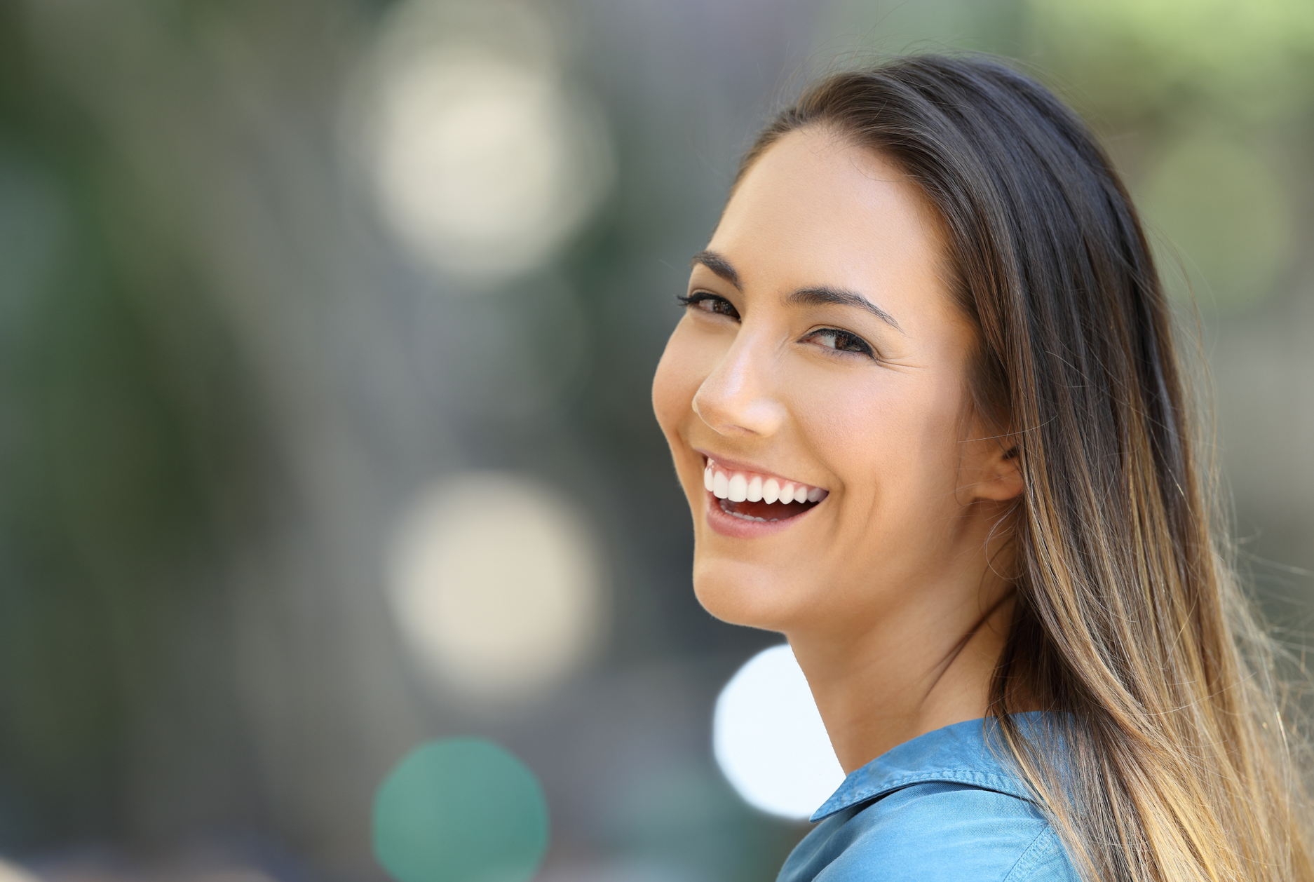 A woman is smiling and looking at the camera with a blurry background.