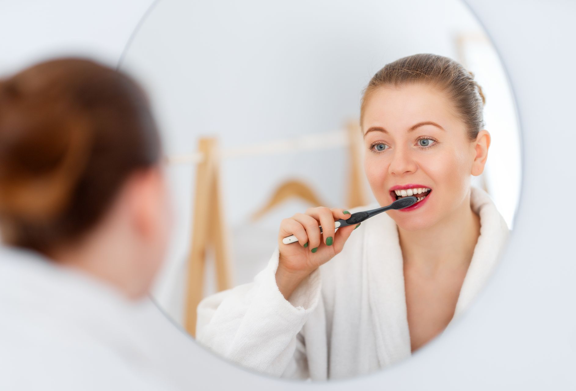 A woman is brushing her teeth in front of a mirror.