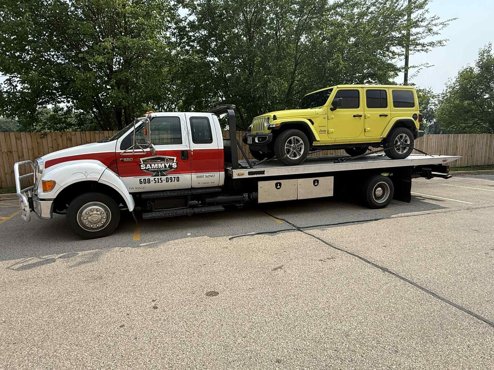 A white and red tow truck with a yellow Jeep on its flatbed, parked outdoors.