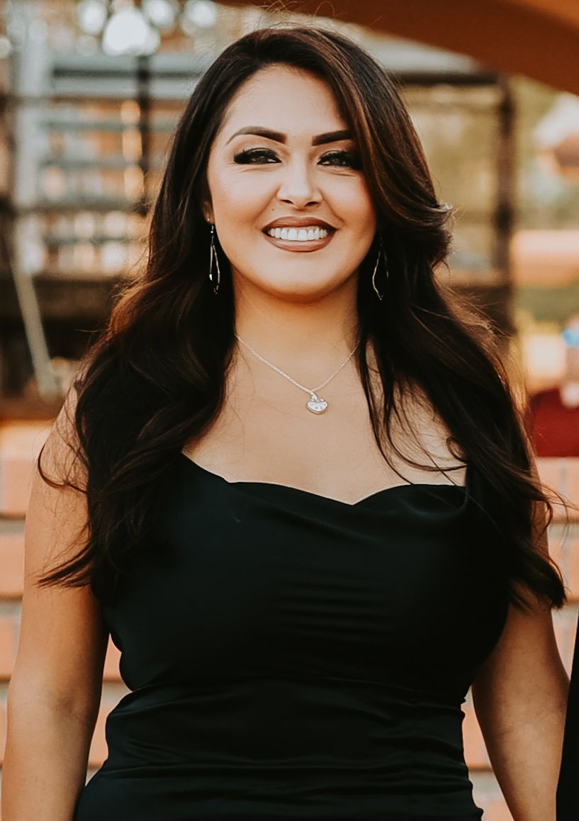 A woman in a black dress and necklace is smiling for the camera.