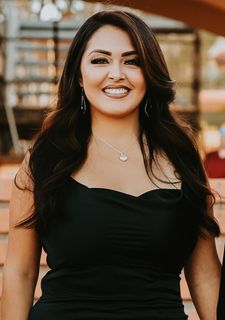 A woman in a black dress and necklace is smiling for the camera.