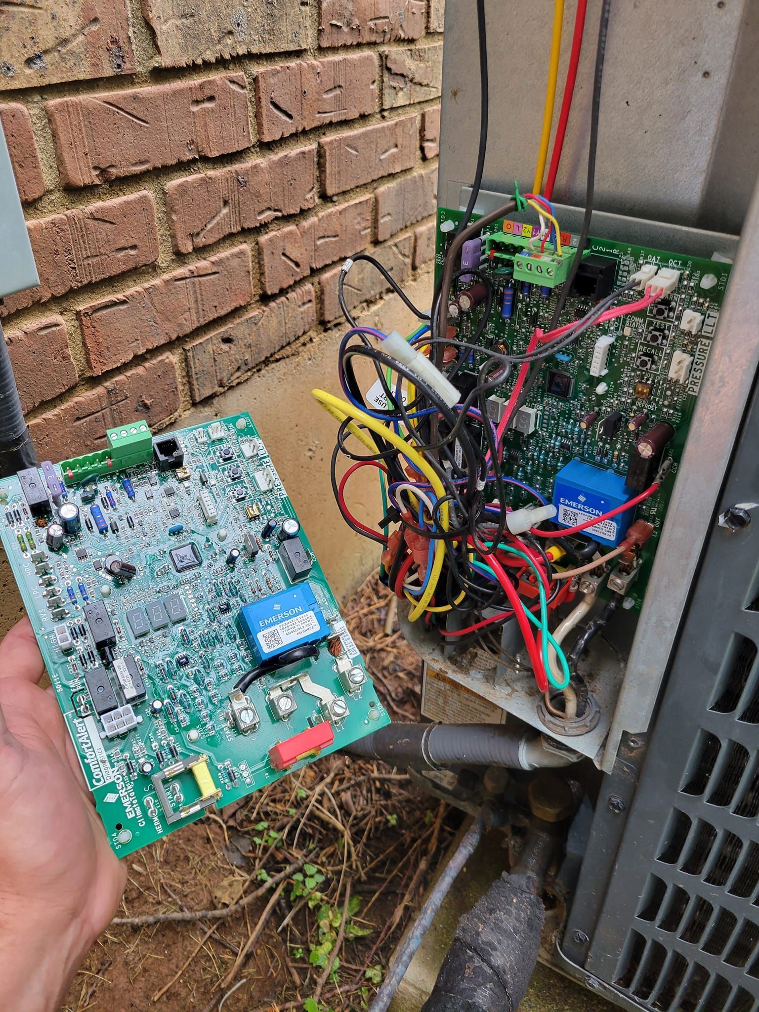 A person is holding a motherboard in front of a brick wall.