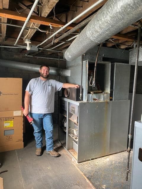 A man is standing in a basement next to a furnace.